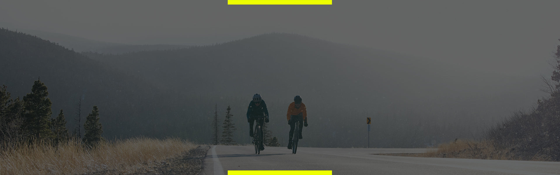 two cyclists riding on a road with mountains in backdrop